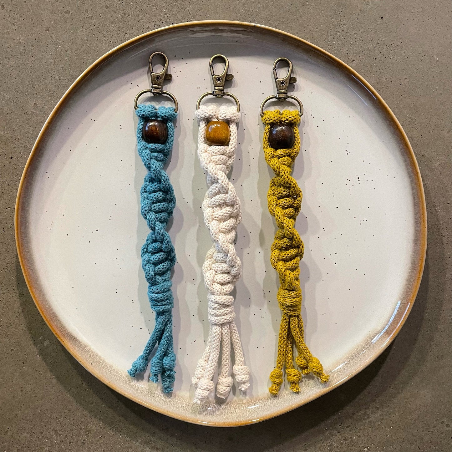 3 Key Chains centered on dinner plate. Twisted style in 3 colors: Teal, Natural White, Spicy Mustard.