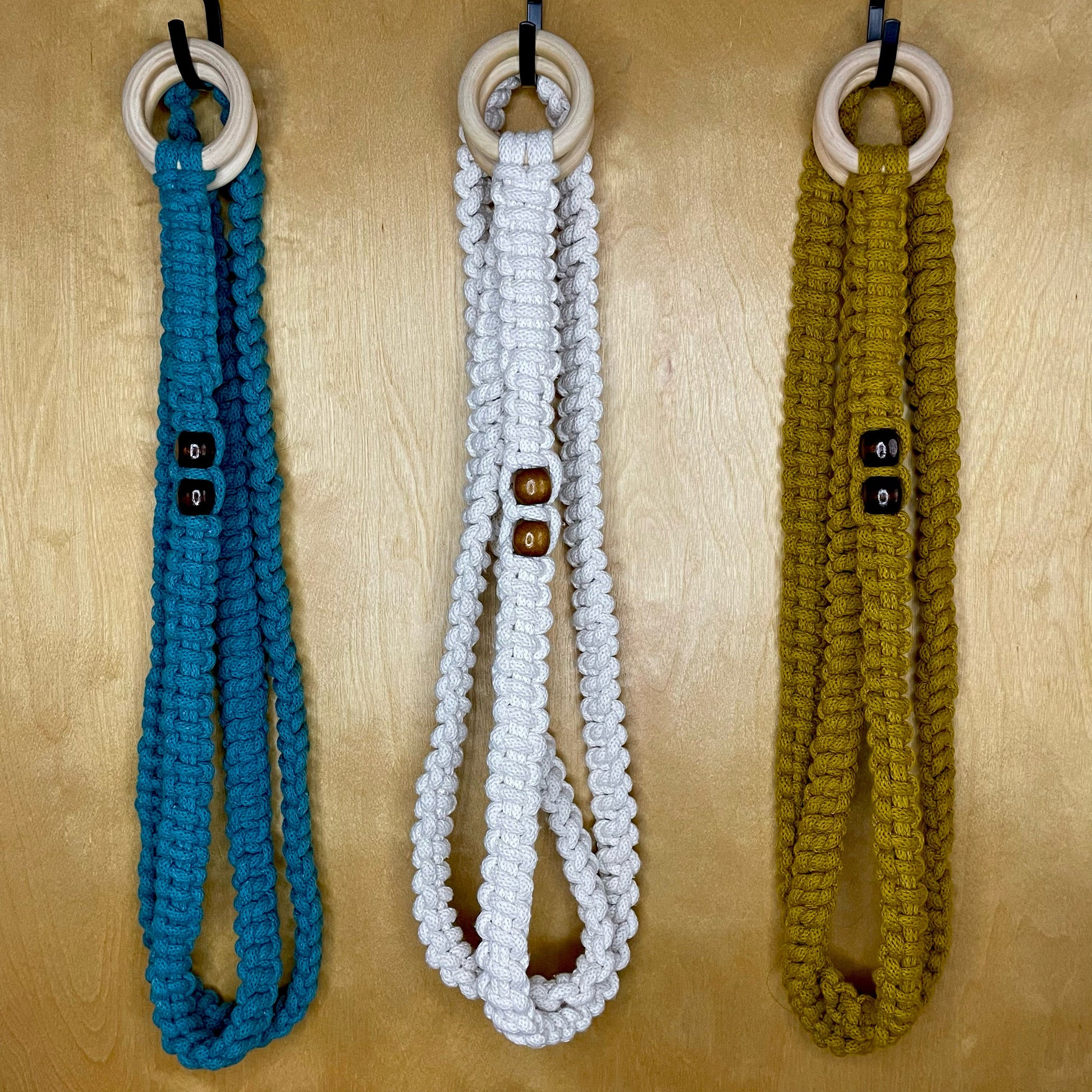 3 yoga straps hanging. Colors shown are Teal, Natural White, and Spicy Yellow